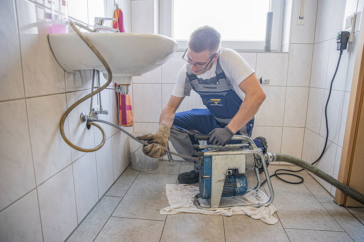 Mitarbeiter von Uhlenbrock Rohrreinigung reinigt Rohr unter Spühlbecken.